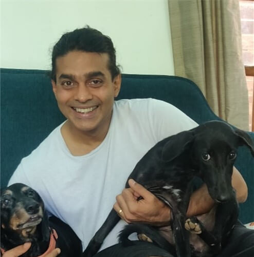 Smiling man with 2 black dogs on his knee.