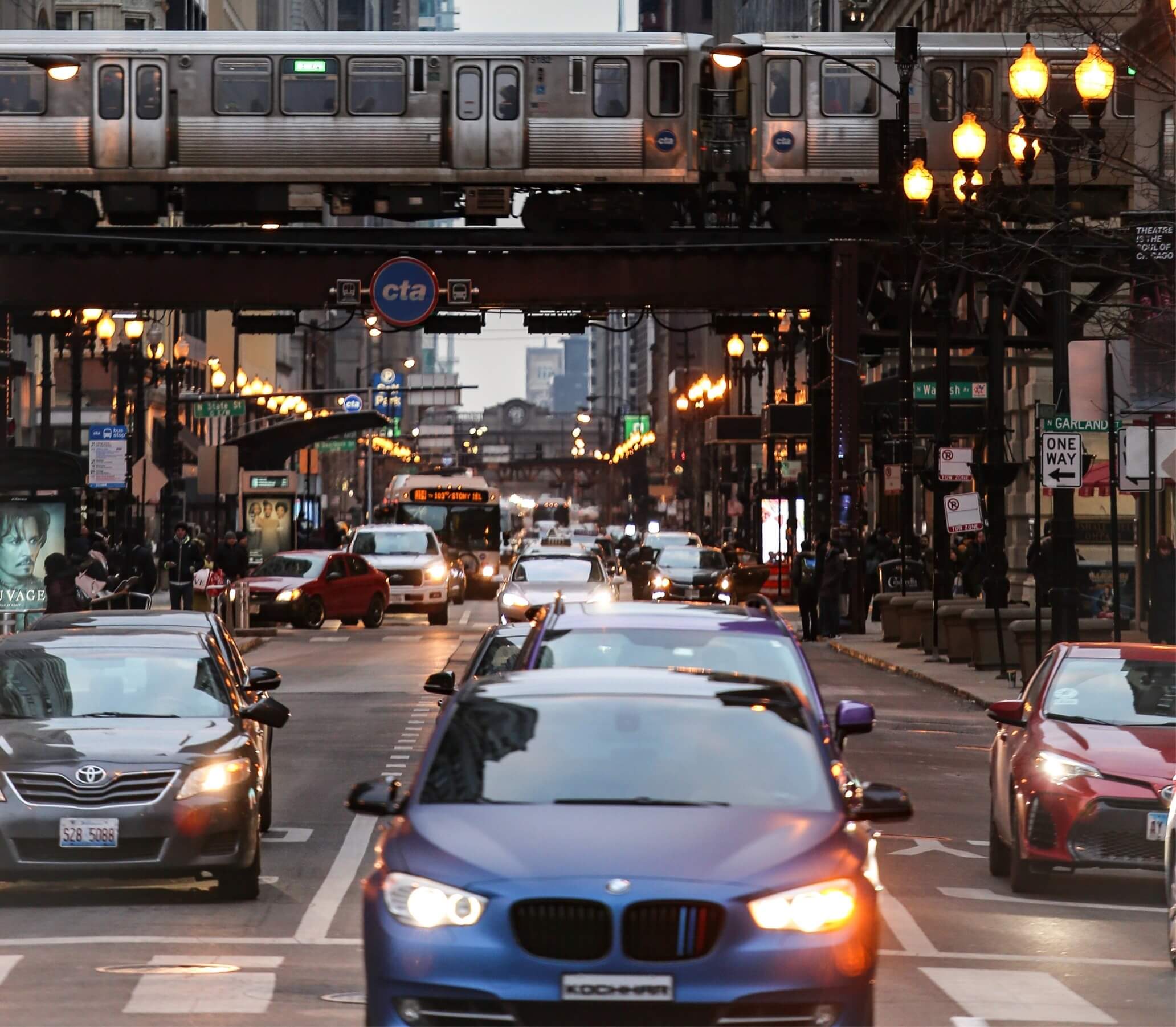 Cars in a busy urban scene with subway train running across the middle of the image.