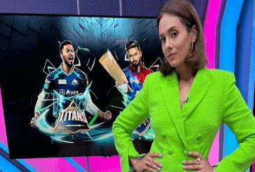 Mayanti Langer, a sports broadcaster from India is wearing a green dress and is standing before a giant TV screen showing an image of two men.