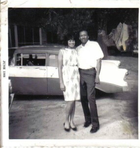 Demar's grandparents in their younger years, posing in front of a classic car.